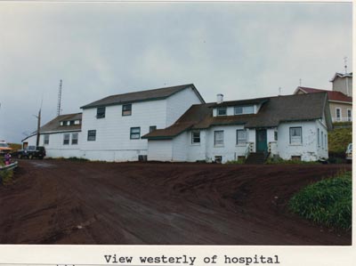 Photo of a westerly view of the hospital, a white building on a dirt road.